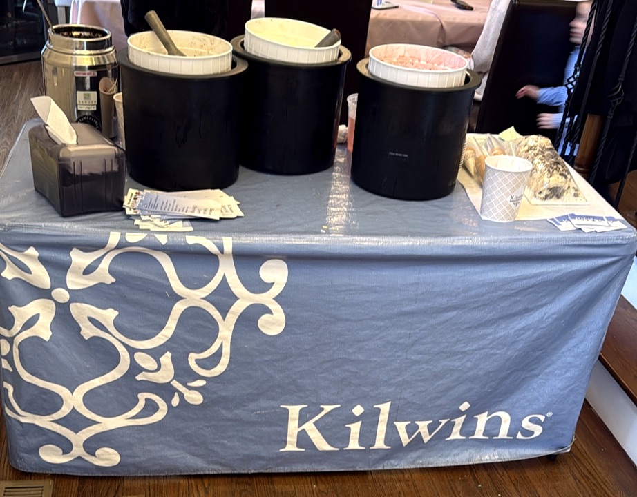 Kilwins branded sundae bar table with ice cream tubs set up at an event